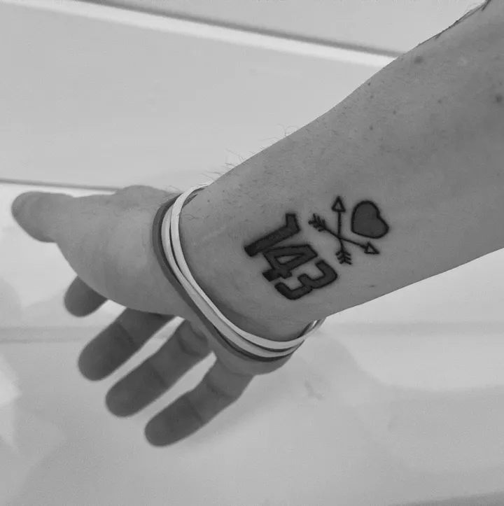 A hand reaching out, 143 and a heart tattooed on the wrist