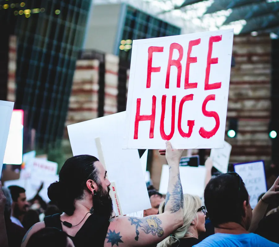 A hand-painted FREE HUGS sign raised above a crowd