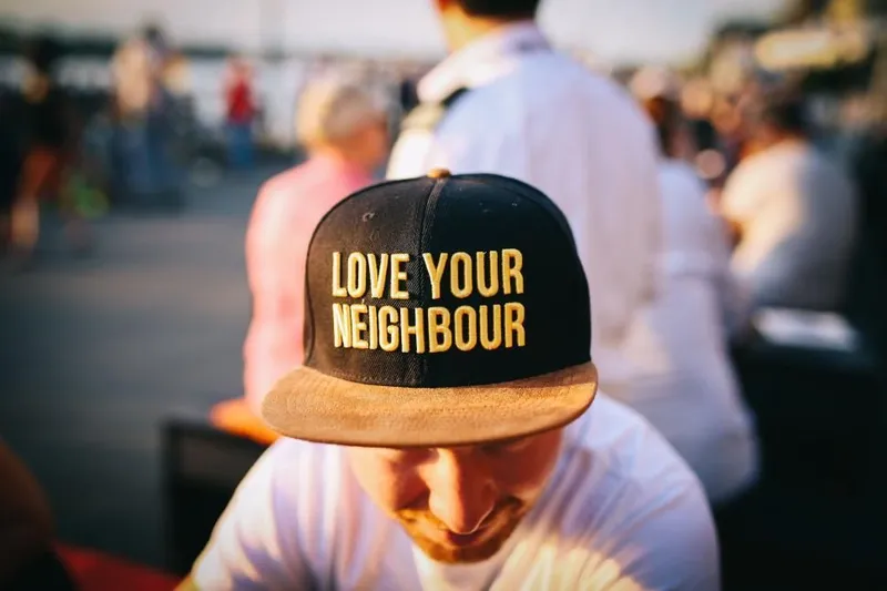 A man in a black cap embroidered with the words Love Your Neighbour in gold